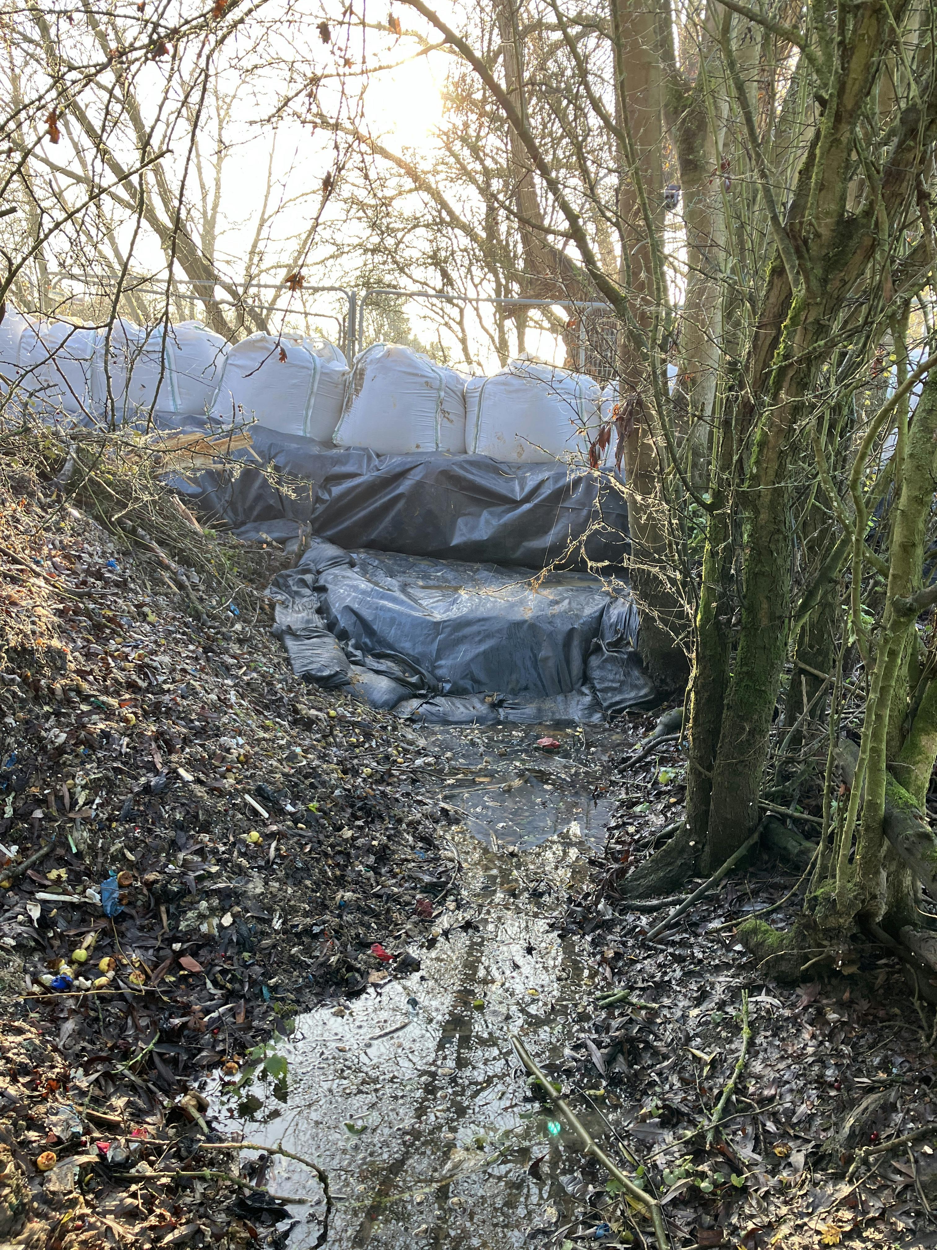 Sandbags blocking a ditch preventing waste behind the sandbags from flowing from the ditch into the river.JPG