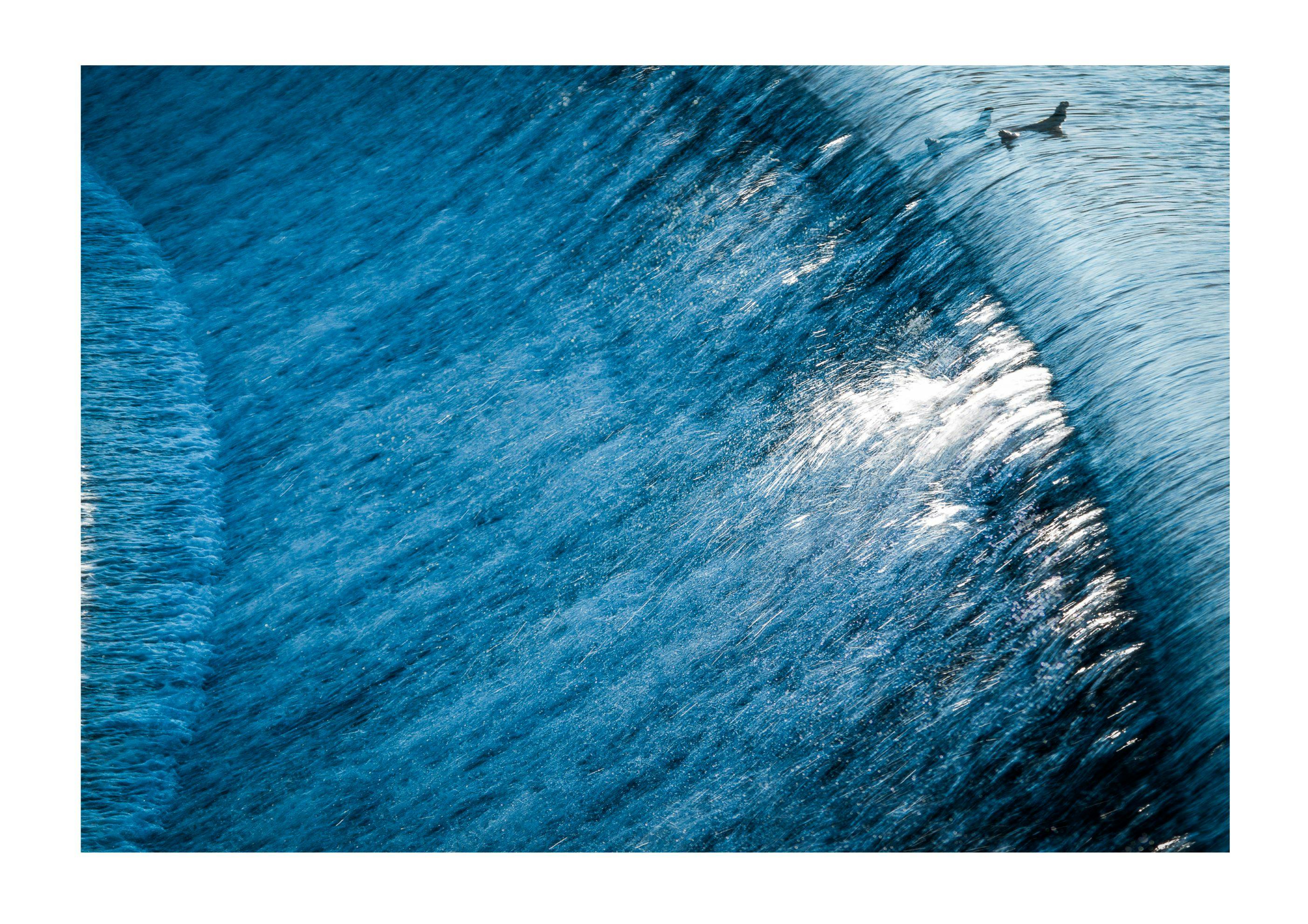 Freemans Weir, a close-up photo of blue-white water flowing down a portion of the face of the extremely long Freeman's Weir which is about 2 meters high and angled at about 45 degrees.  
