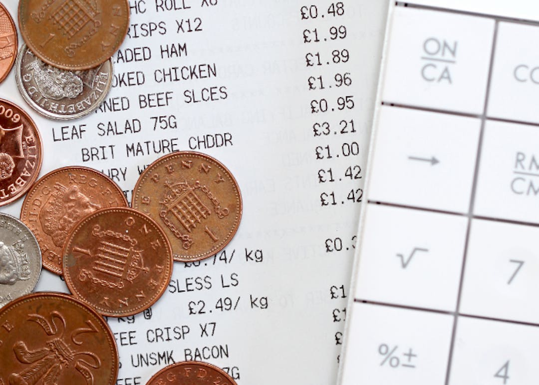 Detail of a groceries receipt, coins and a calculator