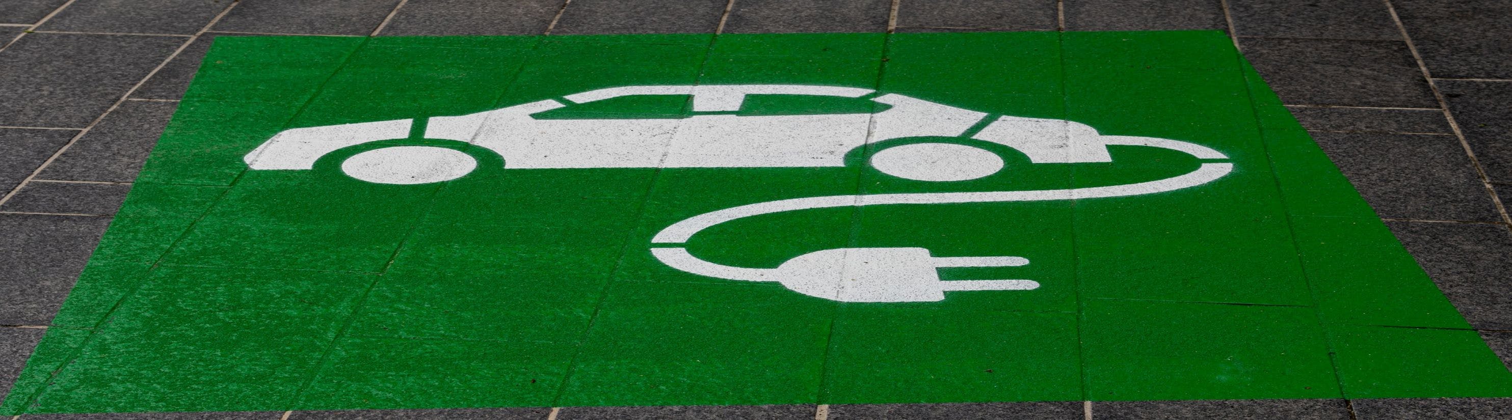 Photo of electric vehicle symbol painted onto road on green background.