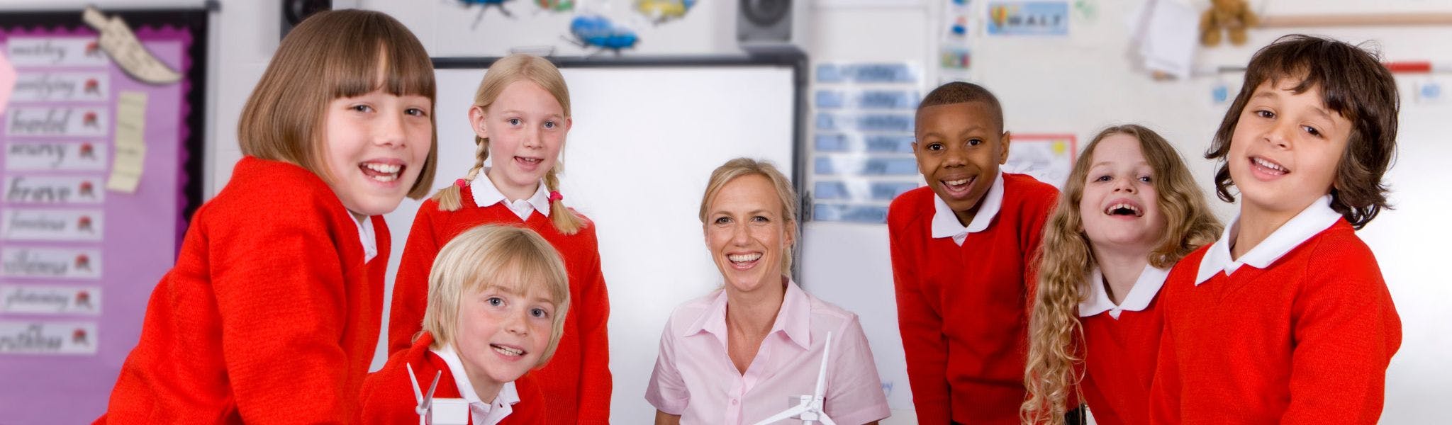 Primary school teacher sitting with pupils at table in a classroom