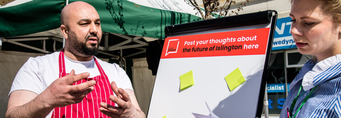 Two people having a conversation standing next to a flipchart with post-it notes stuck on it.
