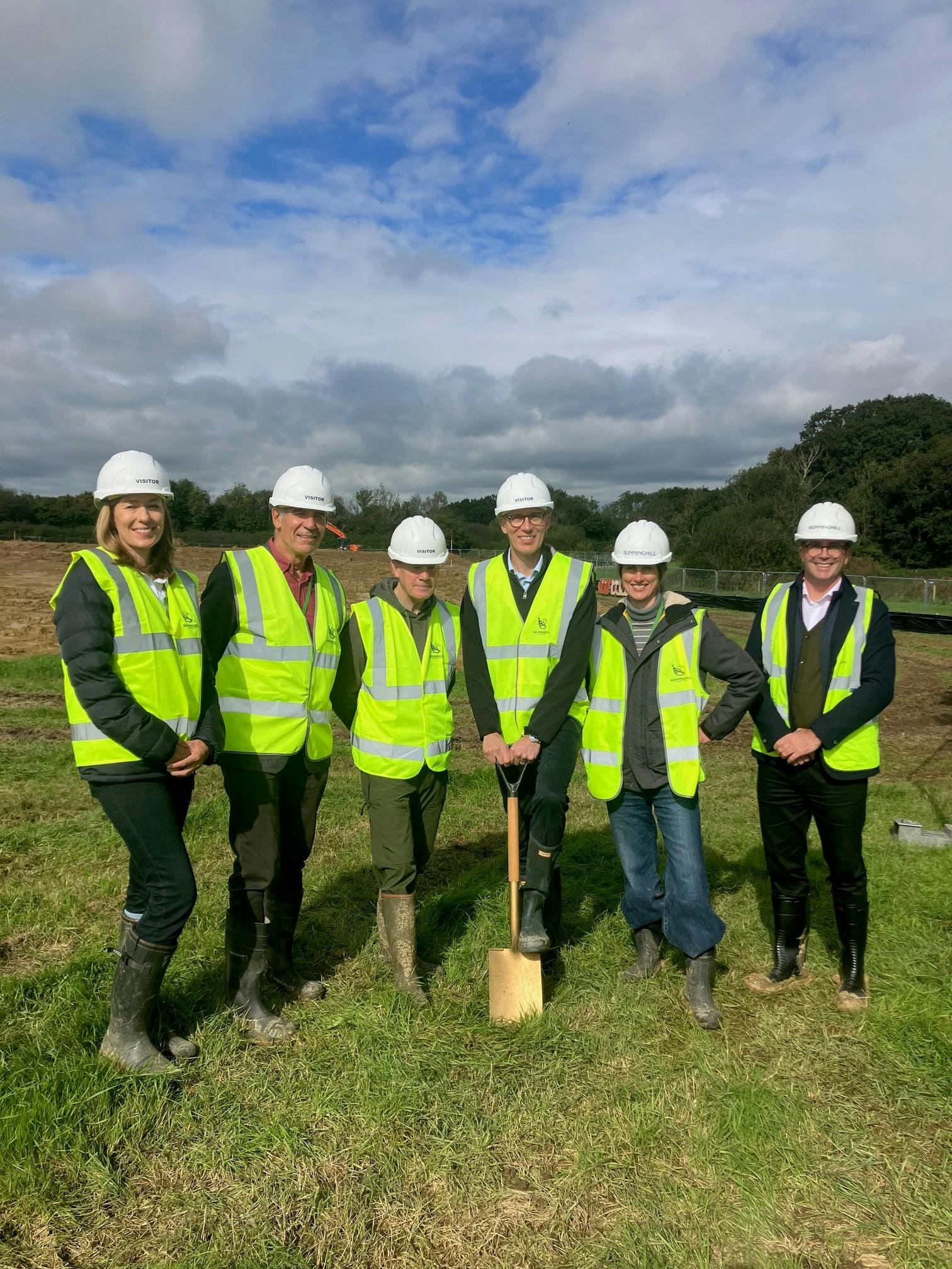 Six people of the sports park project team in high vis jackets and hard hats putting a spade into the ground