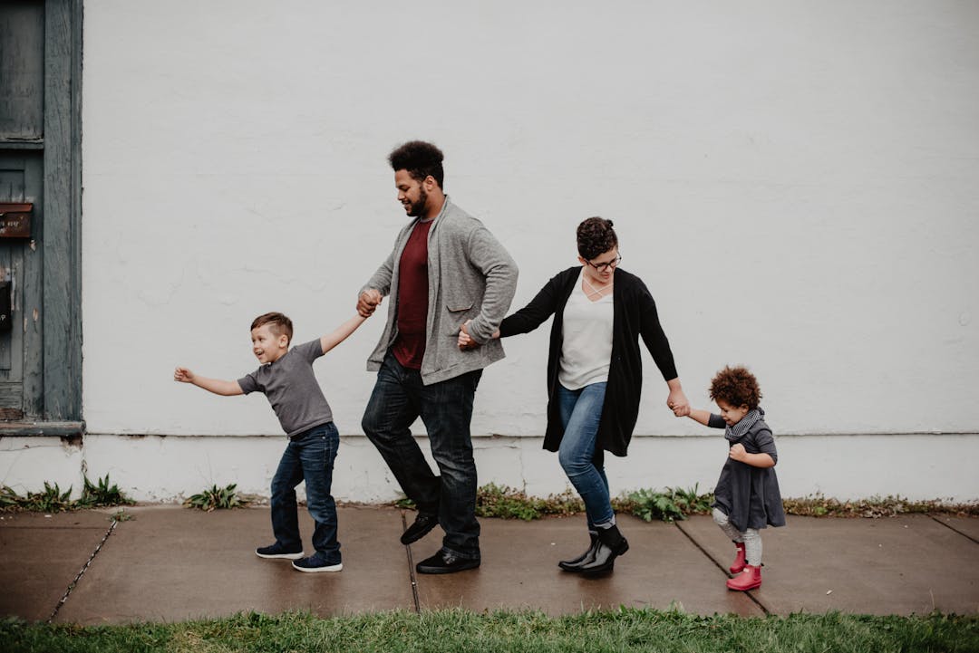 2 adults holding hands with 2 young children walking along a footpath