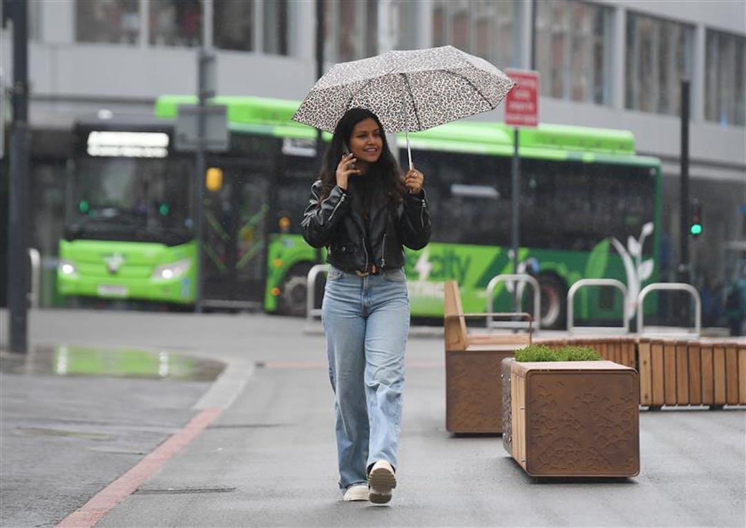 A person walking away from a bus, smiling and talking on the phone, holding an umbrella
