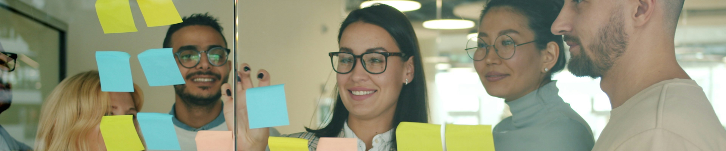 Four people behind a glass wall placing sticky notes on the glass.