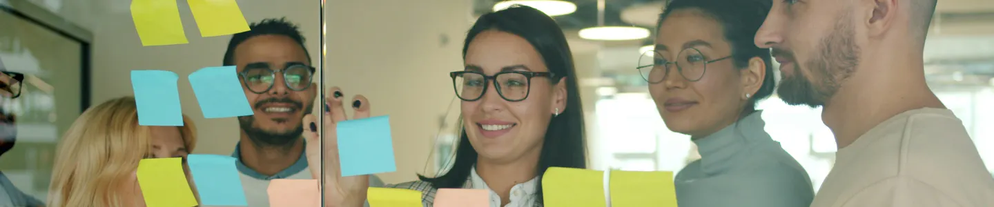 Four people behind a glass wall placing sticky notes on the glass.