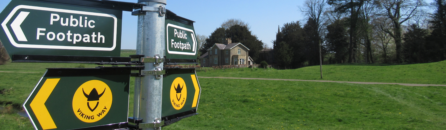 An image of a public footpath sign and background of a field and house.