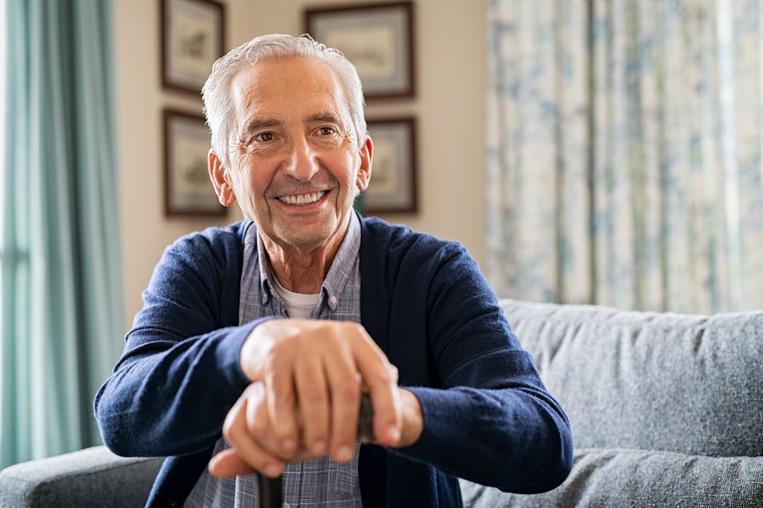 Older man sitting on sofa holding a cane.