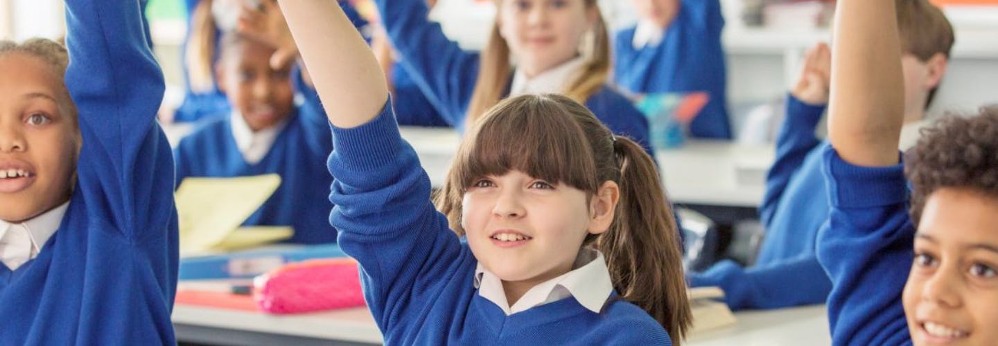 A group of primary school children raising their hands and smiling