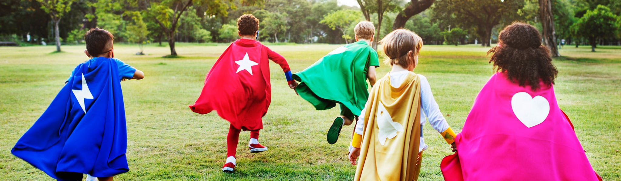 children in colourful capes pretending to superheroes in a park