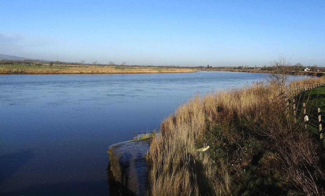 A drone-eye view across Steart Marshes in Somerset with blue skies and sun shining off the water.