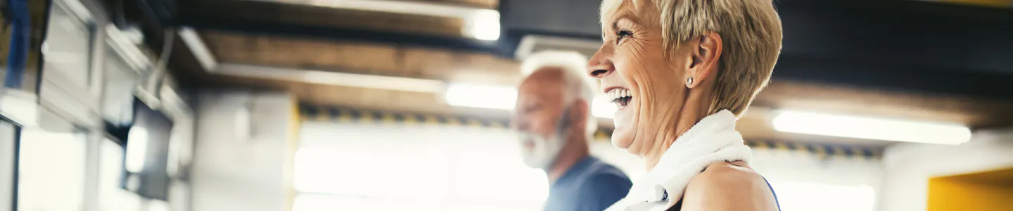 Happy elderly woman and man exercising in gym.