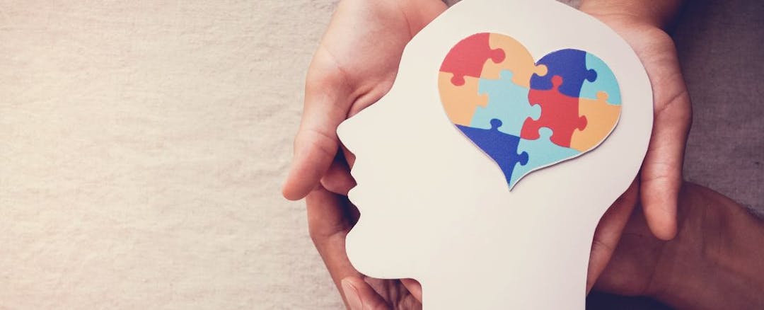 Image of hands holding the silouhette of a head, with a heart shaped puzzle