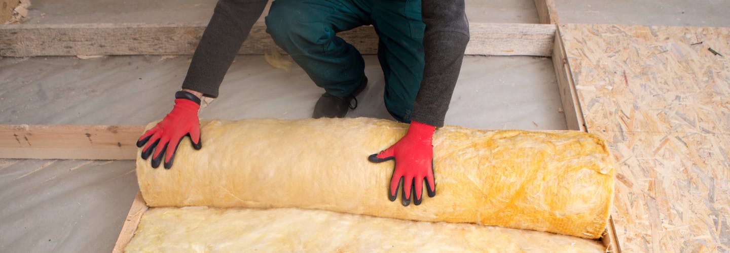 A person wearing protective gloves laying loft insulation 