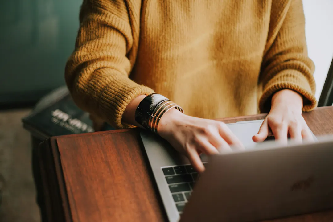 A person in a yellow jumper sat at a desk typing on a laptop