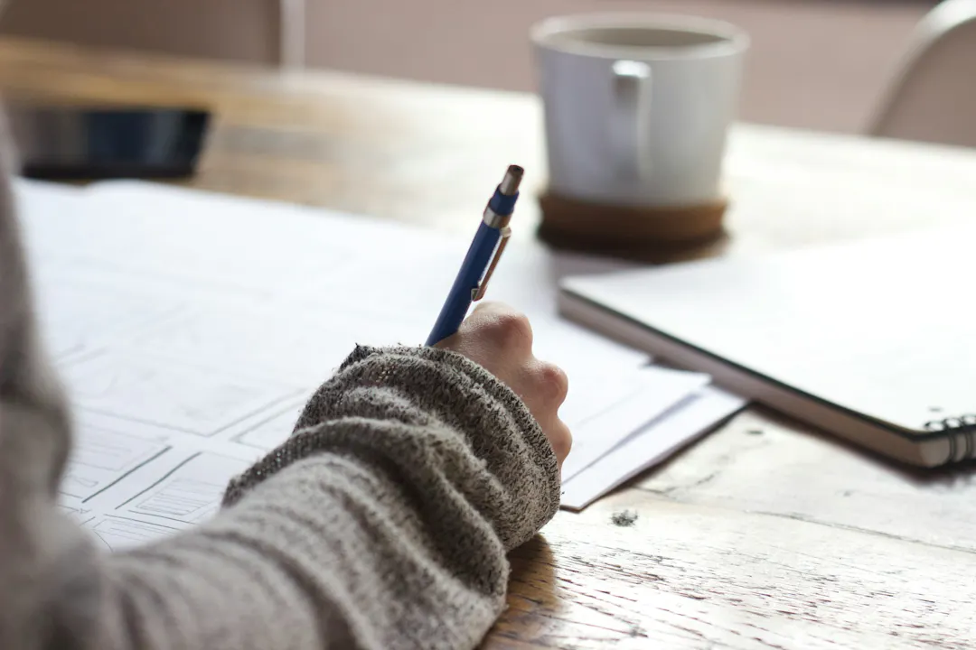 Person at desk with a drink and note books