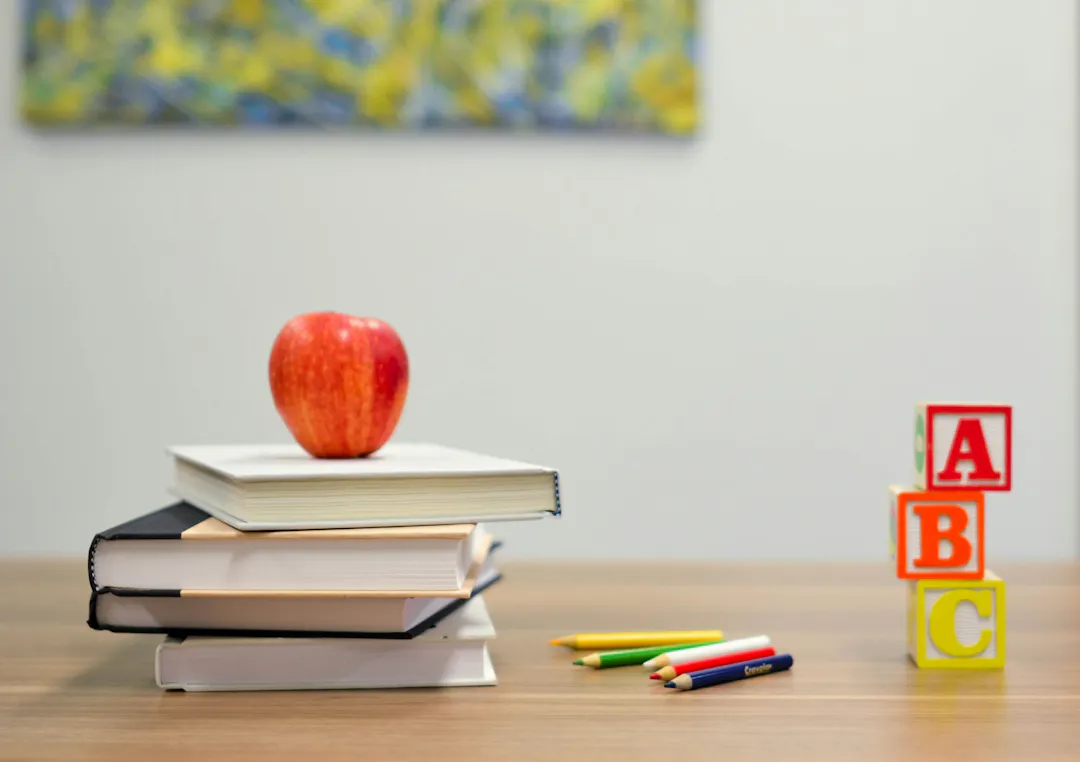 A pile of books, an apple on top and the letters A B and C